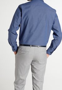 Chemise à carreaux bleue pour homme avec manches longues, associée à un pantalon gris. La chemise est dotée d'un col classique et de poignets à boutons.