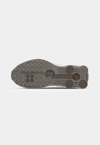 Semelle de sneaker grise en caoutchouc texturé pour l'adhérence, présentant des motifs circulaires et linéaires ainsi qu'un détail de logo central.