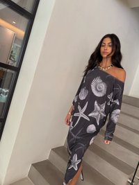 Vestido de manga longa, com ombros à mostra, em cinza escuro com padrões brancos de temática marítima, apresentando uma fenda lateral e uma textura de tecido suave.