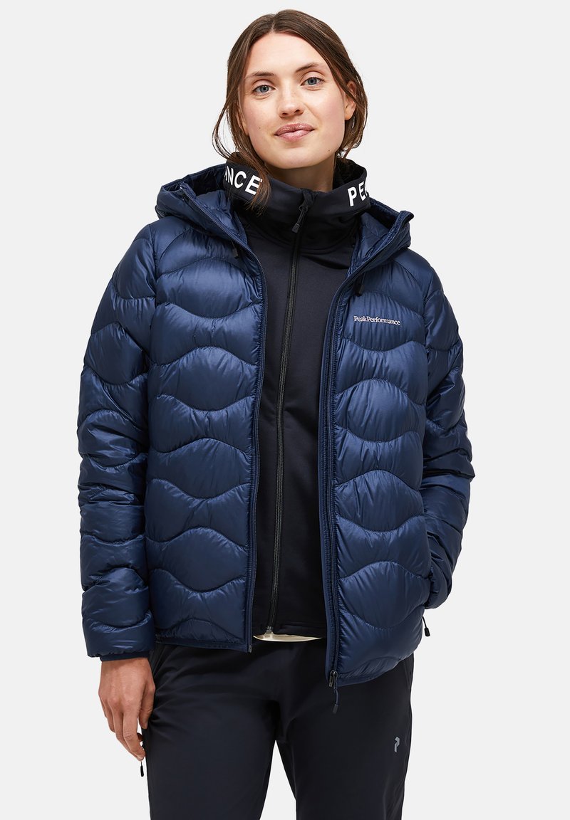 Marineblauer Steppjacke mit gewelltem, gestepptem Design, Kapuze und Reißverschluss. Verfügt über ein Logo auf der Brust und kontrastierenden Kragenbeschriftung.