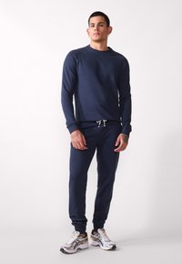 Navy blue sweatshirt with long sleeves and ribbed cuffs, paired with matching joggers featuring a drawstring waist. Sneakers with reflective accents.