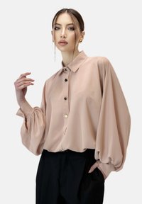 Lichtroze blouse met een kraag, knopen aan de voorkant en volumineuze pofmouwen. Soepele stof met een subtiele glans.
