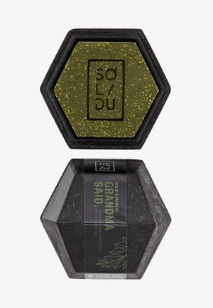 Barra di shampoo solido esagonale in verde con perlature dorate, confezionata in un packaging nero e un'etichetta che dice "GRANDMA SAID" con grafiche di piante.