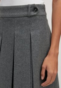 Grauer Wollrock mit gefaltetem Design, glatter Textur und sichtbarem schwarzen Knopfdetail am Bund.
