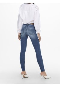 Smala blå denimjeans med en urtvättad finish och två bakfickor, kombinerat med en vit blus med broderade detaljer och ballongärmar.