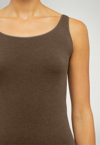 Brun bomullstank topp med rundad halsringning och smala axelband. Tyget har en slät yta och en åtsittande form, lämplig för lager-på-lager.