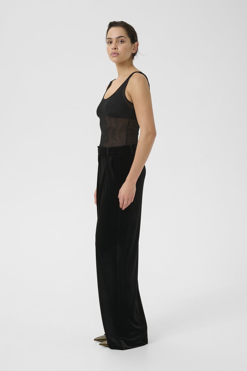 Black, sheer tank top with ribbed texture paired with high-waisted black velvet trousers. Pointed gold heels add metallic detail.