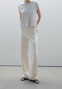 Vaaleanharmaa lyhythihainen paita, rento malli; yhdistettynä kermaisiin leveisiin farkkuihin, sileä pinta ja mustiin litteisiin sandaaleihin. Minimalistinen muotoilu.