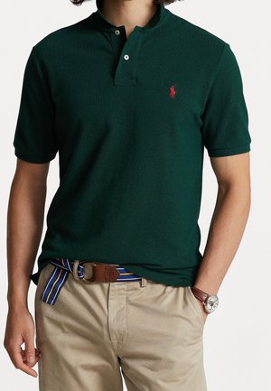 Donkergroen poloshirt met een kraag met twee knopen, met een klein rood logo. Gecombineerd met beige broek en een multicolor gestreepte riem.