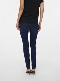 Smale mørkeblå jeans med middels høy midje, baklommer og detaljer med søm. Brukes med svart skjorte og høye hæler.