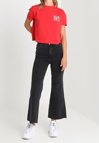 Camiseta corta roja con el logo "HOME BOY", combinada con jeans negros acampanados y zapatillas blancas. Tejido suave y corte relajado.