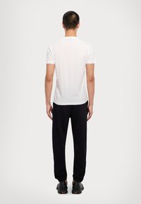 Hvit t-skjorte med korte ermer, sammen med svarte joggebukser med avslappet passform og elastiske mansjetter, sett fra baksiden.