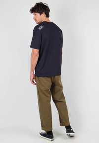 T-shirt bleu marine à manches courtes et col rond, associé à un pantalon olive légèrement ample. Présente un petit logo sur le t-shirt.