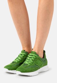 Baskets en daim vert et nylon avec des surfaces texturées, des lacets plats et une semelle en caoutchouc blanche avec un motif en zigzag.