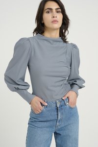 Gray puff-sleeve top in a smooth fabric, featuring a high neckline and gathered waist detail, paired with high-waisted blue denim jeans.