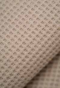 Tejido beige texturizado con un patrón de diamantes en relieve, que muestra una apariencia suave y tejida. Destaca la calidad táctil del material.