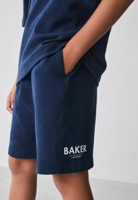 Marineblå bomuldsbukser med sidelommer, med en hvid "BAKER" logo på kanten, glat tekstur og afslappet pasform.