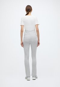 Kerge, valge lühikeste varrukatega särk, mis on kombineeritud hallide ribidega lõhestatud pükstega. Pükstel on kõrge vöökoht ja kergelt kulunud äär.