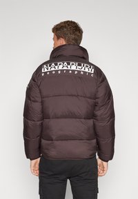 Brun puffjacka med kviltat mönster, har en stor vit logotyp med texten "NAPAPIJRI geographic" på ryggen.