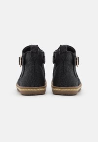 Černé kotníkové boty s texturovanou koženou povrchovou úpravou, s bočním zipem a akcentem v podobě přezky, a hnědou gumovou podrážkou s detailním prošíváním.