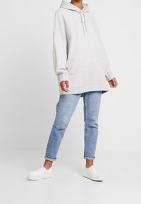 Szary, oversize'owy hoodie z kapturem i sznurkiem, w połączeniu z jasnoniebieskimi dżinsami o prostym kroju i białymi trampkami. Prosty, casualowy design.