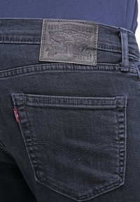 Jeans in denim scuro con una etichetta in pelle sulla parte posteriore con testo in rilievo, un classico design a cinque tasche e cuciture a contrasto sulle tasche.