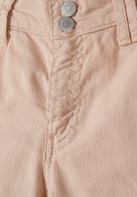 Tissu en denim rose clair avec deux fermetures à boutons argentés, présentant des coutures visibles et des détails de texture. Gros plan de la zone de la taille.