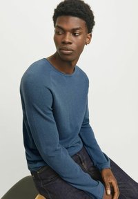 Blå textured langærmet skjorte med rund halsudskæring, parret med mørke jeans. Materialet virker blødt med et tætsiddende design og ribbede manchetter.