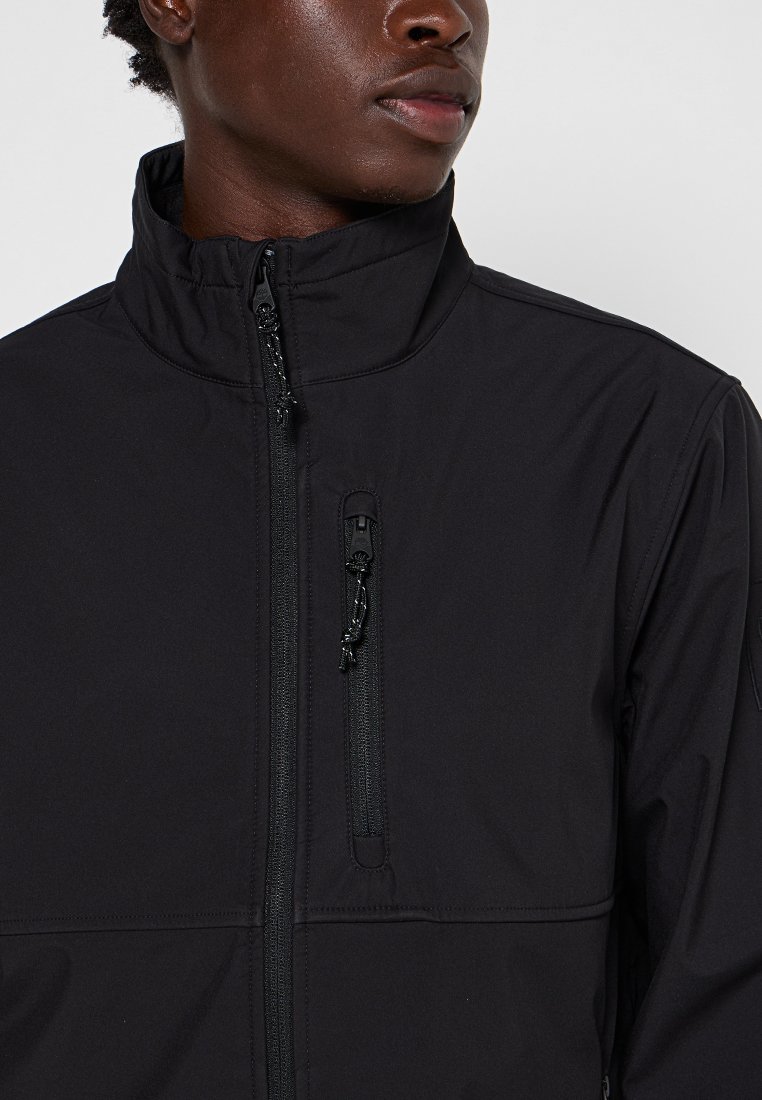 Zwarte softshell jas met een hoge kraag, een rits aan de voorkant en een borstzak. Heeft een gladde textuur en een minimalistisch ontwerp.