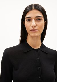 Schwarzes Strick-Polohemd mit Kragen und Knopfleiste. Der Stoff sieht glatt aus und hat eine feine Textur.