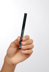 Penna eyeliner nera tenuta in mano, con un design cilindrico elegante, etichetta in testo bianco e finitura opaca con punta affilata.