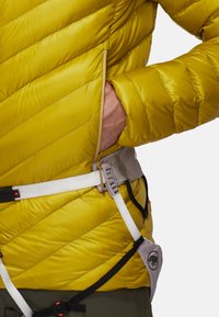 Veste rembourrée jaune, matelassée, avec des rayures diagonales, équipée d'une poche latérale et maintenue par un harnais avec une ceinture grise et des accents noirs.