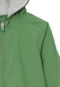 Giacca impermeabile verde con cappuccio interno grigio, cerniera frontale e una leggera accentuazione azzurra sulla manica. Tessuto liscio e resistente.
