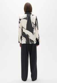 Black and white abstract printed blazer with long sleeves, paired with loose black trousers. Smooth fabric with a relaxed fit.