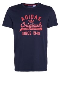 Tmavě modré bavlněné tričko s nápisem „ADIDAS Originals“ červenou barvou, s vintage fontem a logem tří pruhů na hrudi.