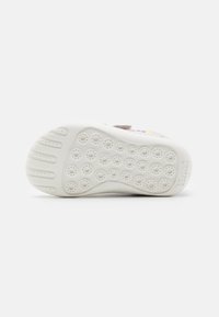 White rubber shoe sole with circular indents, featuring raised ridges for grip. Lightly textured with a clean design and brand logo imprint.