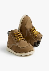 Braune Lederstiefeletten mit gelben Schnürsenkeln, weißen Nähten und einer Gummisohle. Sie verfügen über eine runde Zehenpartie und einen gepolsterten Schaft.