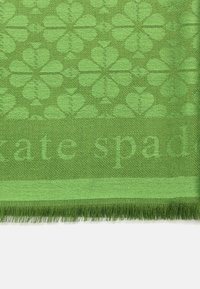 Green woven scarf featuring a floral pattern and fringe edges, with a subtle "kate spade" logo. Textured fabric gives a rich feel.