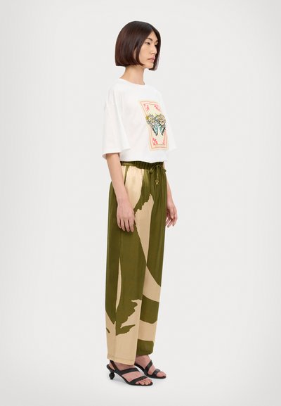 Camiseta blanca de gran tamaño con estampado de mariposas, combinada con pantalones de pierna ancha de patrón verde oliva y beige. Sandalias negras con tiras.