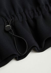 Tejido negro con frunces elásticos y un ajustador de toggles negro en contraste, con una textura suave y un diseño fluido y suave.