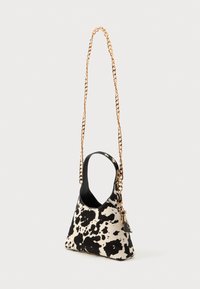 Borsa a forma triangolare con stampa a macchie bianche e nere, con tracolla in catena dorata e interno nero liscio. Include un piccolo dettaglio con etichetta.