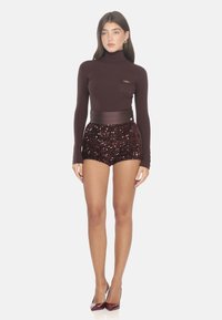 Golf bordeaux a coste con tasca e mini pantaloni a paillettes marroni; a vita alta, abbinati a tacchi bordeaux coordinati.