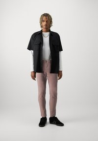 Camisa negra de manga corta sobre una camisa blanca de manga larga, combinada con jeans ajustados rosas y zapatillas negras. Diseño simple y casual.