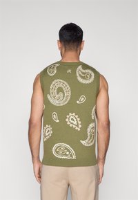 Žalias rankovių megztinis su kremine paisley rašto juosta, ribotu kaklu ir apačia. Lygus tekstūra, prigludusi forma. Be matomų detalių ar akcentų.