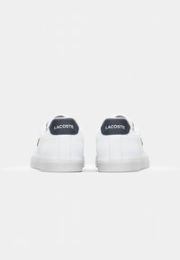 White sneakers with a smooth leather finish, navy heel accents, and gold logo detail. Features a round toe and flat rubber sole.