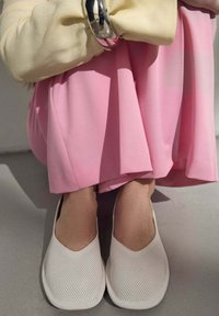 Bílé nazouvací boty s perforovaným designem, s kulatou špičkou a měkkou, pružnou podrážkou. Nosit se se světle růžovou sukní.