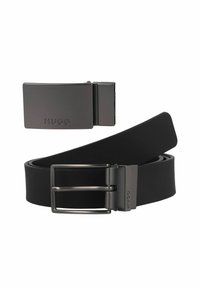 Zwarte leren riem met een matte afwerking, voorzien van een metalen gesp met een rechthoekige vorm en een gegraveerd logo. Zachte textuur, minimalistisch ontwerp.