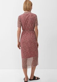 Vestido de estampado floral rojo con mangas de 3/4, material transparente, cinta en la cintura y largo hasta la mitad de la pantorrilla. Se llevan sandalias planas negras.