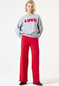 Sweatshirt gris avec "LOVE" en lettres rouges en gras, associé à un pantalon rouge à taille haute et jambes larges avec des coutures avant. Chaussures noires visibles.