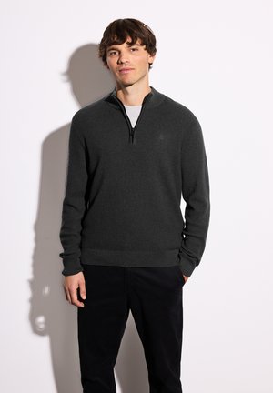 Mørkegrå pullover-sweater med halv-zip krave, ribbet tekstur og lange ærmer, parret med sorte bukser.